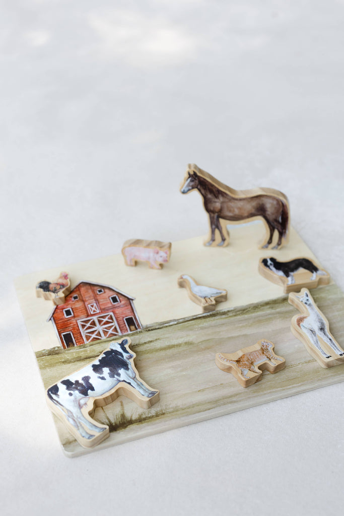 The Farm Animals Wooden Puzzle: A Tabitha Paige Puzzle is a charming educational toy for toddlers, featuring farm animal pieces—including a horse, pig, cat, duck, dog, cow, goat, rooster—and a red barn, all arranged neatly on a light beige surface.
