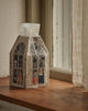 The Coral & Tusk Haunted House Tissue Box Cover, featuring embroidered spooky characters in the windows, sits on a wooden windowsill beside cream-colored curtains.