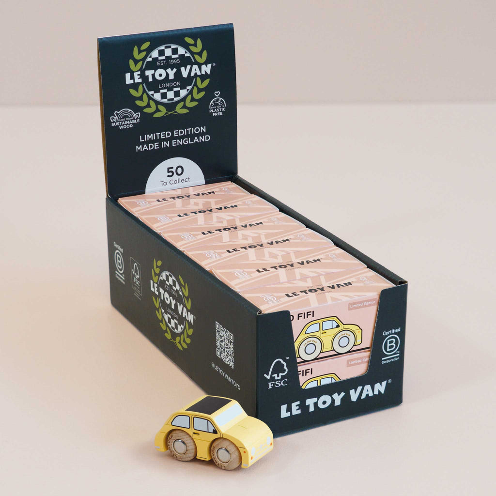 A display box of Le Toy Van limited edition toy cars features the No. 10 GT60 Fifi—a charming yellow wooden car labeled “Fifi”—prominently in front. The box announces “50 to collect” and showcases eco-friendly certification logos, highlighting these classic miniatures made in England as perfect vintage toys for both collectors and children.