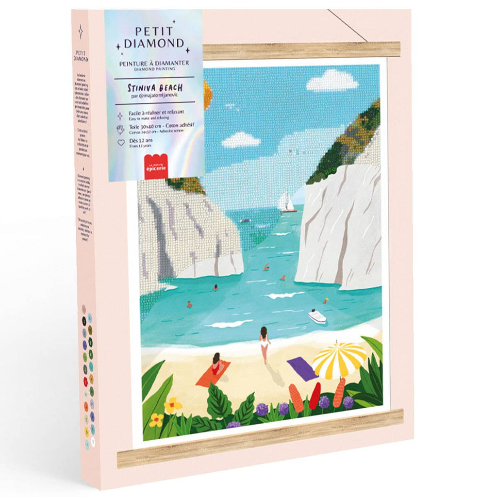 The Diamond Painting Kit - Stiniva Beach by Maja Tomljanovic features a vibrant illustration of people enjoying a sandy Mediterranean cove with white cliffs, turquoise water, colorful towels, umbrellas, and lush plants.