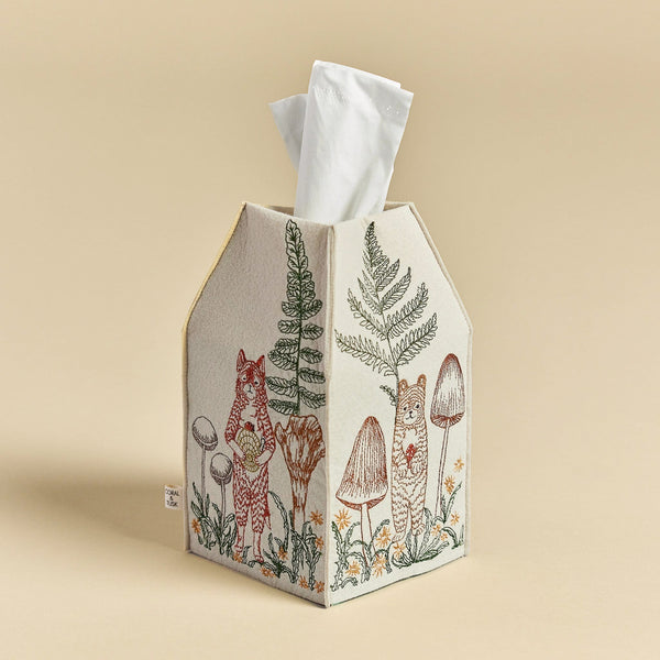 An embroidered Coral & Tusk Mushrooms and Ferns tissue box cover designed to look like a house, featuring woodland scenes with a deer, mushrooms, and ferns on a beige background.