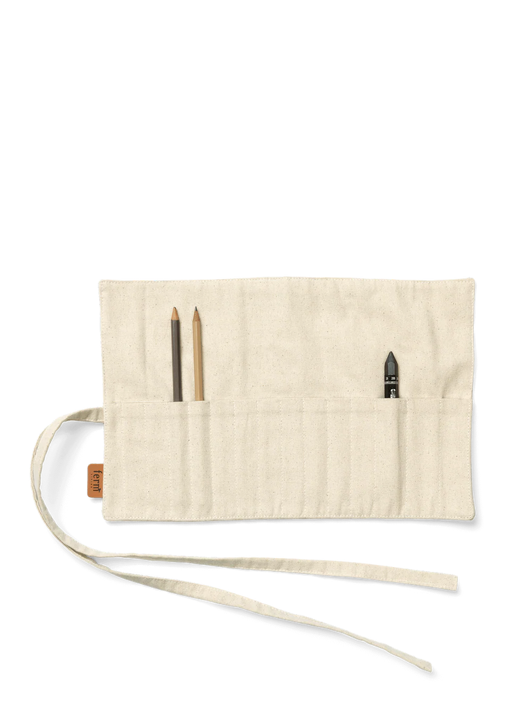 The Ferm Living Ally Pencil Wrap in off-white, made from organic cotton with multiple pockets, is shown partially open on a white background holding two pencils and a black sharpener.