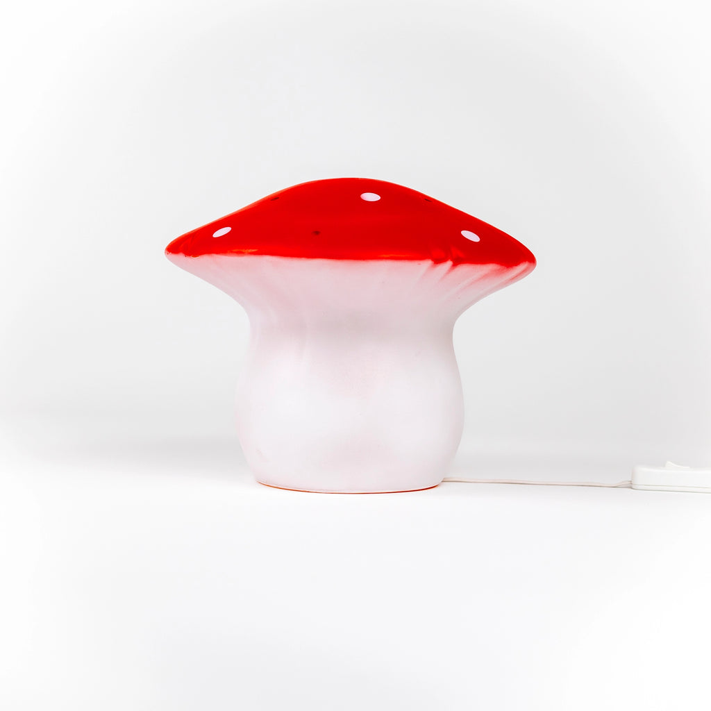 The Red Mushroom Lamp is a whimsical night light with a red cap featuring white spots and a white stem, shown on a plain white background with its power cord visible.