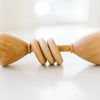Two Wooden Baby Rattles, made in USA, touching fingertips in a soft, minimalist setting with a bright, blurred background.