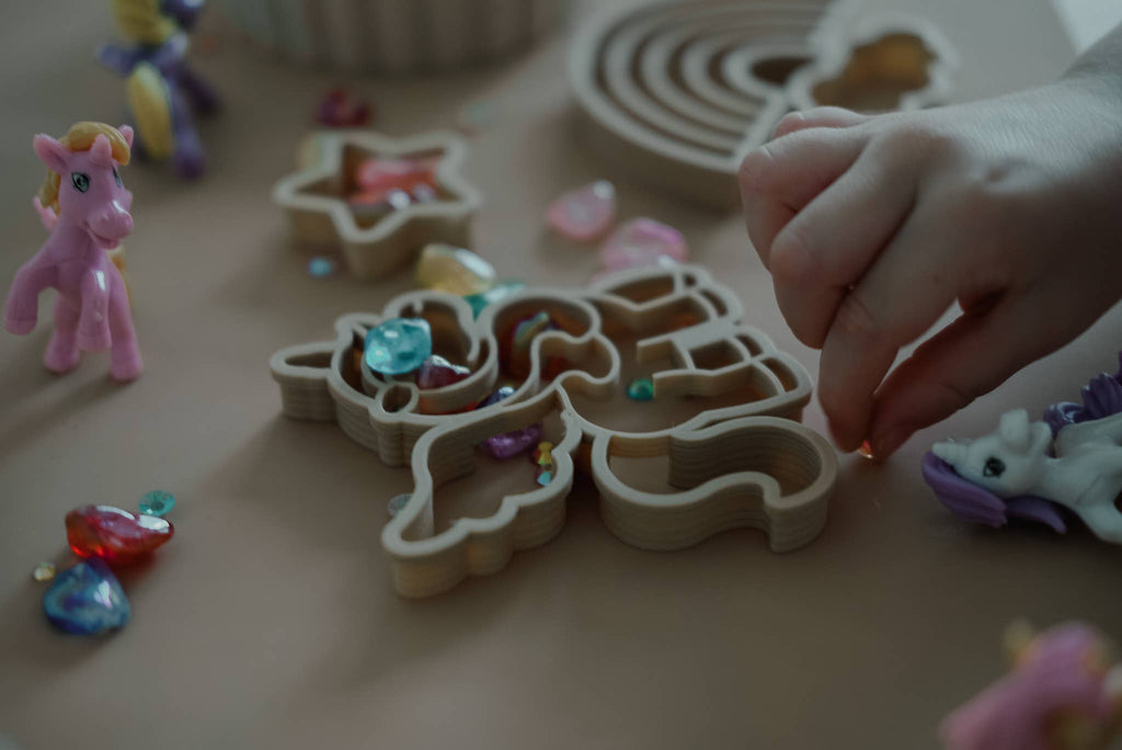 A child’s hand arranges vibrant gems into a unicorn-shaped puzzle on the table, while the Unicorn Cutter Set – Eco Playdough Tool and small toy ponies invite creative sensory play among scattered gems.
