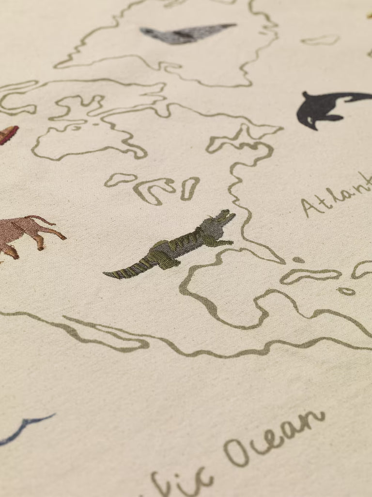 A close-up of the Ferm Living The World Textile Map - Off-white, showing an embroidered animal map of North America with stylized creatures, labeled "Atlantic Ocean," and detailed coastlines for a unique organic cotton wall decor.