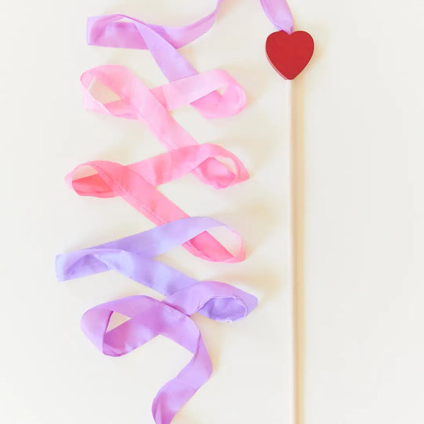Two intertwined Sarah's Silk Large Heart Streamer Wands in soft pink and purple hues with a heart-shaped topper on a stick, positioned against a pale background.