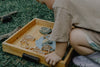 A child kneels on grass, playing with the Pond Life Cutter Set – Eco Playdough Tool and decorated cookies in a wooden tray.