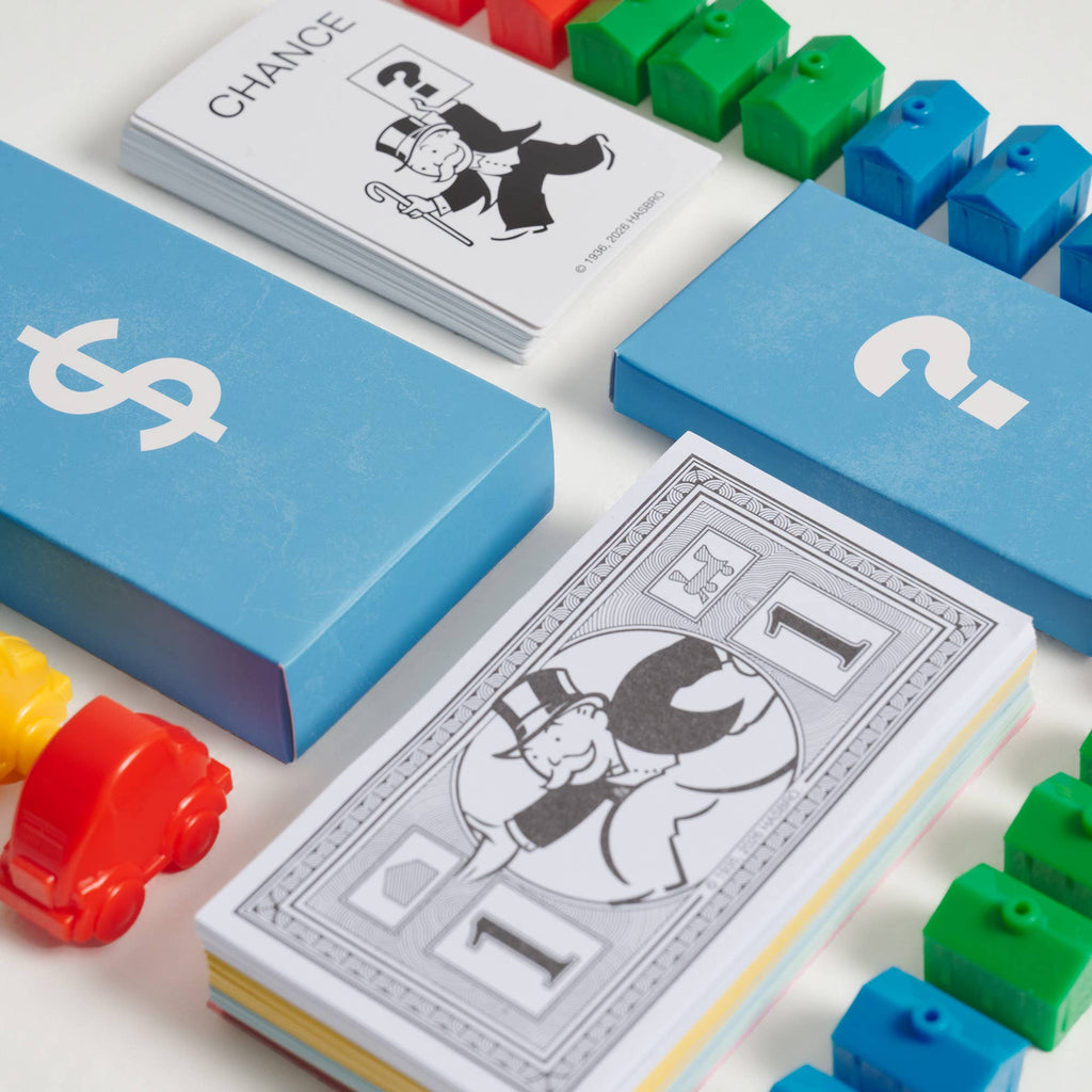 Monopoly Junior Vintage Bookshelf Edition components, including Chance cards, a stack of one-dollar bills, colored plastic houses, and player tokens arranged on a white surface.