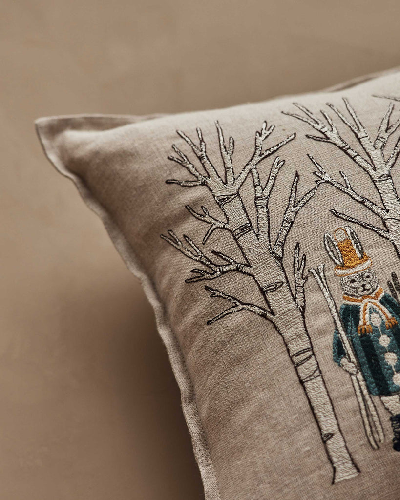 The Coral & Tusk Aspen Skiers Pillow features embroidered bare trees and a snowman in a yellow hat and scarf with skis, making it a whimsical winter decor accent.