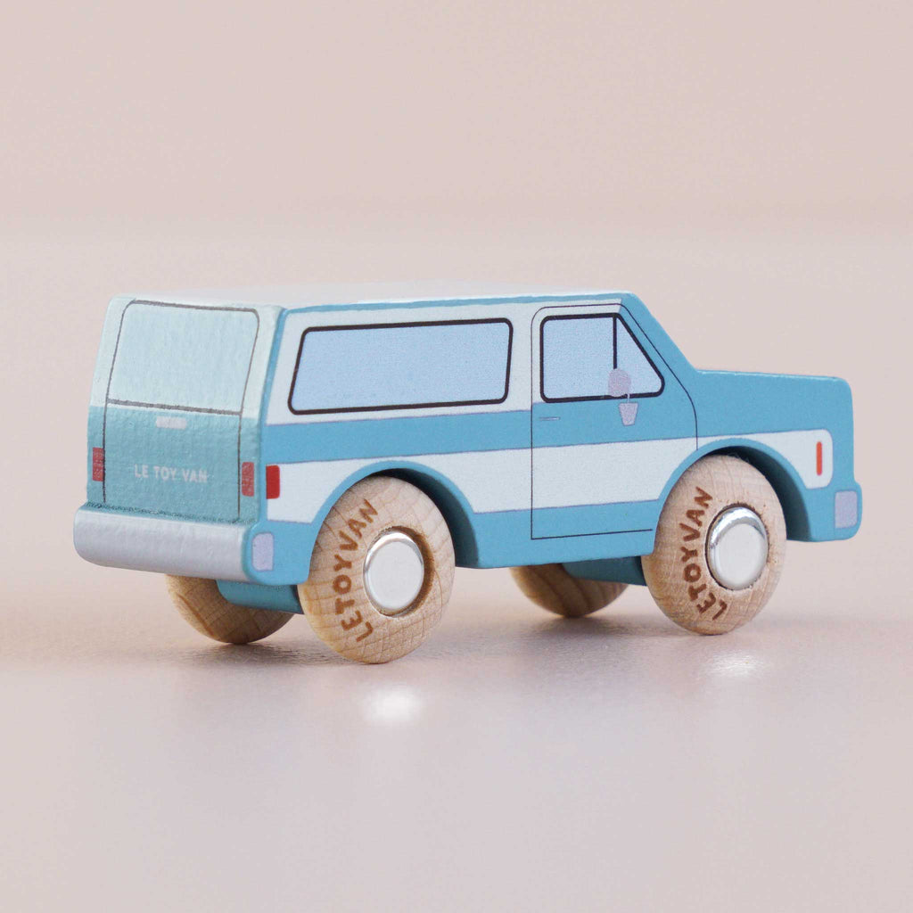 A blue-and-white wooden SUV toy car, crafted in England and named “No. 31 GT170 Chuck,” features black windows, wooden wheels labeled “Le Toy Van,” and sits against a light pink background—perfect for igniting off-road adventures in imaginative play.