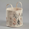 The Coral & Tusk Full Moon Masquerade Bucket is a fabric storage basket with two handles, featuring illustrated designs of children in various Halloween costumes—including a mummy, ghost, pumpkin, skeleton, and animal outfits—set against a light gray background adorned with bare trees and an owl.