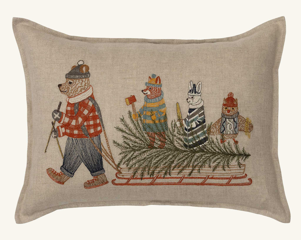 The Coral & Tusk Christmas Tree Sled Pillow features embroidered animals in winter attire—a skiing bear pulls a sled with an owl, rabbit, and fox among pine branches—bringing whimsical charm to your holiday decor.