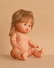 The Minikane Baby Doll (13") - Yzé sits upright on a beige surface with brown pigtails, blue eyes, and pink lips. Made in Spain, this anatomically correct doll comes unclothed; clothing sold separately.