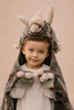A young child with light eyes and short hair smiles in the Costume - Triceratops Dino, featuring horns and paw-like mittens, against a neutral background.
