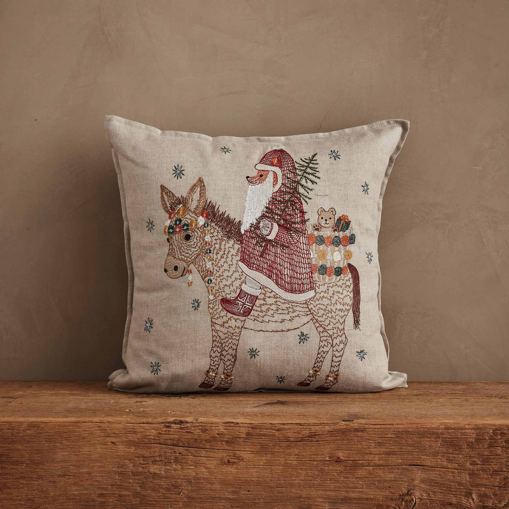 The Christmas Donkey Pillow features a charming Santa Donkey with gifts and a tiny owl on its back, surrounded by blue snowflakes—perfect festive decor for your home.