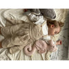 A toddler with light brown hair sleeps on a cream blanket, cuddling the Senger Naturwelt Cuddly Animal - Seahorse, with a pink seahorse grain pillow nearby. The child wears a beige pinafore dress over a white shirt.