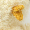 Close-up of the Cuddle + Kind Baby Bouclé Chick (Buttercup), featuring curly cream fur and a small yellow knitted beak—ideal for fans of collectible stuffed animals and hand-knit baby animal toys.