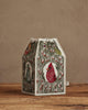 The Coral & Tusk Birdhouse Tissue Box Cover, featuring embroidered birds and floral designs, sits on a wooden surface against a beige wall.
