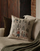 A beige couch features a green throw blanket and two pillows—one solid green and the Coral & Tusk Winter Fun Pillow, embroidered with woodland animals sledding and skiing—ideal for cozy winter or holiday decor.
