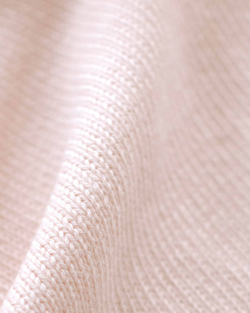 Close-up of the Cuddle + Kind Organic Cotton Baby Bear Lovey in blush—a soft, textured, hand-knit fair trade gift with gentle folds and a cozy waffle knit pattern, perfect for babies.