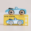 A blue wooden toy car with a “LE TOY VAN” label sits on a yellow box that reads “No. 1 GT10 Justin | Made in England,” featuring icons for sustainability, UK-made craftsmanship, and child-safe paint—making this classic car a delightful keepsake for any collection.