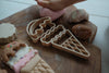A child's hand presses pink dough next to the Ice Cream Cutter Set - Eco Playdough Tool, featuring wooden ice cream playdough cutters and pretend ice cream toys on a wooden board—perfect for imaginative sensory play.