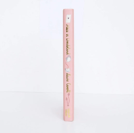 The image shows the spine of a pink "Alice in Wonderland | Collector's Edition" hardcover book decorated with illustrations of a teapot, teacup, and heart.