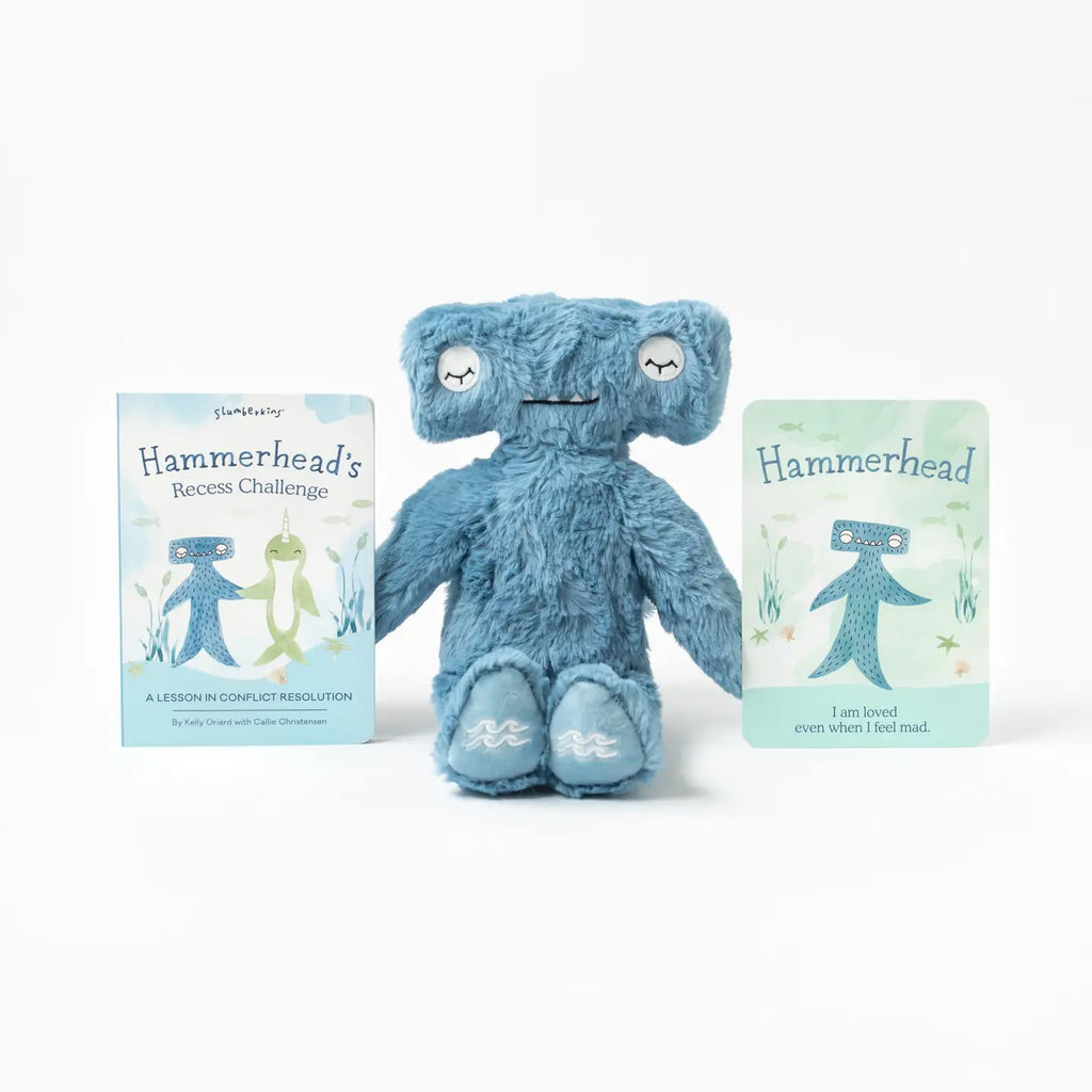 A **Slumberkins Hammerhead Kin + Lesson Book - Conflict Resolution** is centered between two illustrated cards. The left card features a hammerhead shark and a turtle with the text "Hammerhead's Recess Challenge." The right card shows the toy with the text "I am loved even when I feel mad," emphasizing emotional regulation for kids.