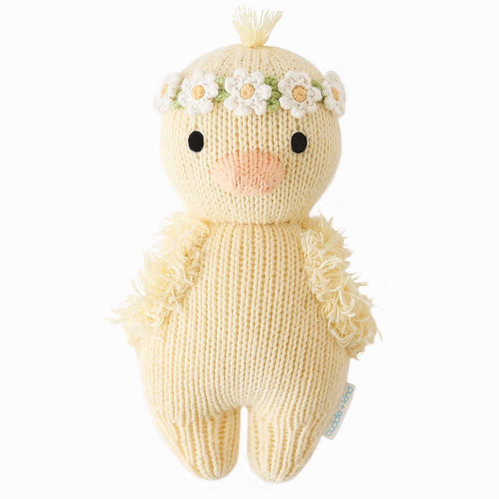 Hand-knit from Peruvian cotton yarn, the Cuddle + Kind Baby Duckling (Ivory Floral Crown) features a peach beak, black eyes, ivory flower crown, fluffy wings, and a light blue tag—an heirloom-quality plush for any collection.