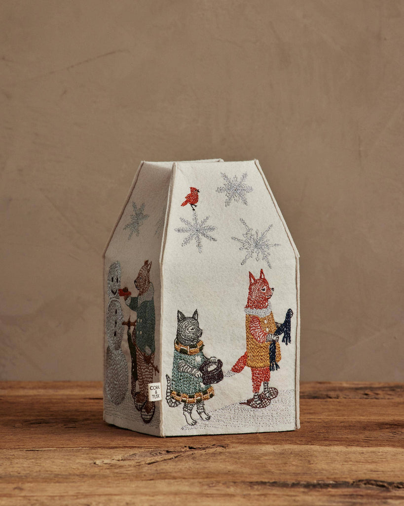 The Coral & Tusk Snow Day Tissue Box Cover features a house-shaped design with embroidered animals in winter attire, snowflakes, and a red bird on beige fabric—an adorable accent for your seasonal decor.