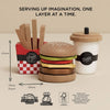 The Gourmet Hamburger Set (ships in one week) includes a layered burger, fries in a red box, and a drink cup with straw—all made from sustainable wood. Black text appears above; eco-friendly icons and measurements are shown below.