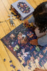 A child assembles the vibrant Courting Critters 500 Piece Puzzle on a wooden floor, with a stuffed toy and the puzzle box nearby—perfect inspiration for creating or gifting this charming, animal-themed puzzle for Valentine’s Day.