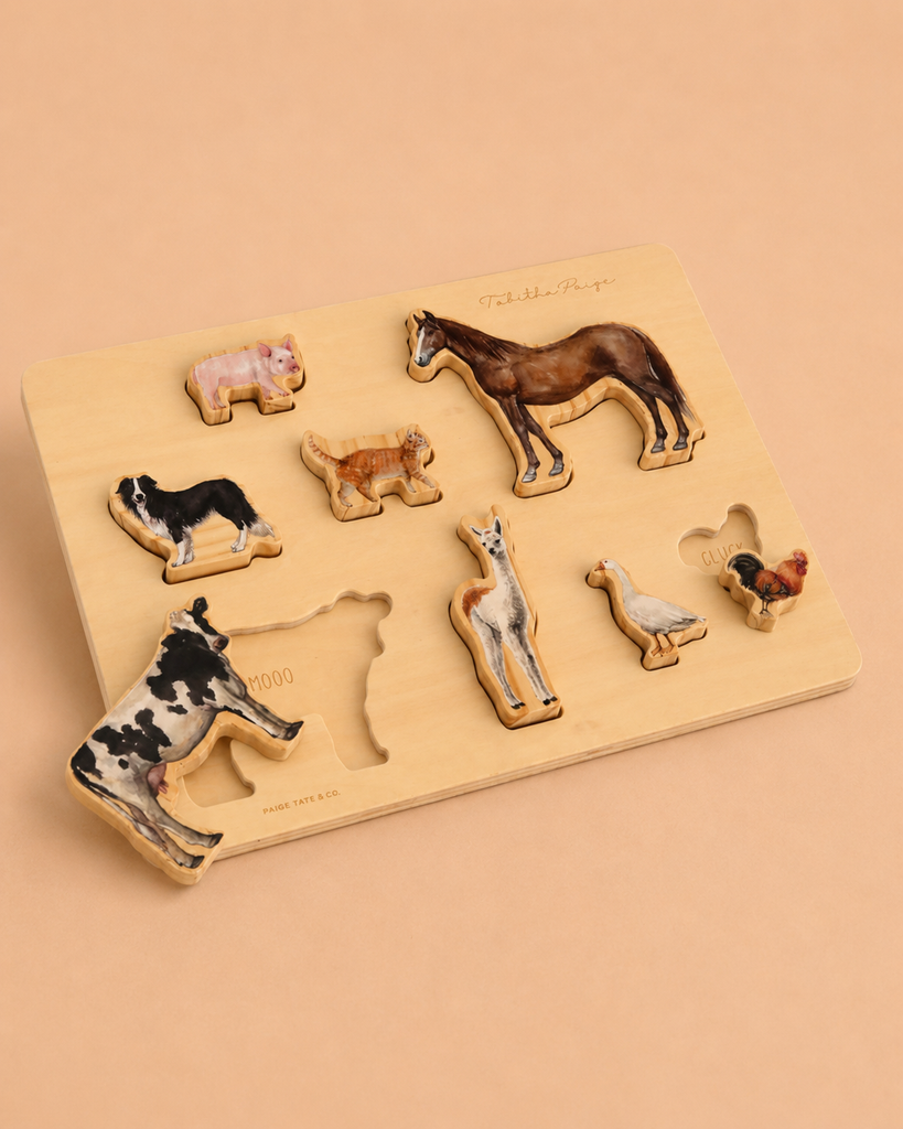 A Tabitha Paige Farm Animals Wooden Puzzle showcases farm animal pieces—cow, pig, horse, sheep, goat, duck, and chicken—on a beige background. This charming educational toy is perfect for toddlers. In this scene, the cow piece is placed outside its slot.