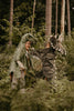 Two children play in a lush forest, surrounded by greenery. One wears the Costume - T-Rex Dino as a cape, while the other sports a gray dinosaur outfit with spikes.