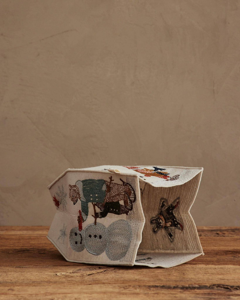The Coral & Tusk Snow Day Tissue Box Cover, featuring embroidered snowmen, a reindeer, and a star, adds festive charm to your snow day decor on any wooden surface or against a neutral beige wall.