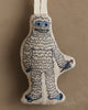 The Coral & Tusk Yeti with Candy Cane Ornament features a smiling yeti embroidered in white and blue, holding a candy cane—an adorable, whimsical addition to your Christmas tree.