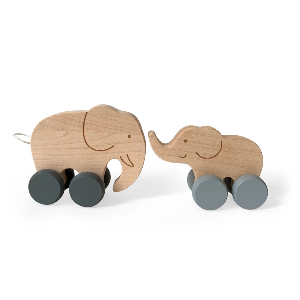 Two **Wooden Mom and Baby Elephant Push Toy Set** with smiling faces, each on four grey wheels. The larger elephant faces the smaller one, mirroring its pose. Made of light wood with a minimalist design, these toys are free of harmful chemicals and perfect for developing fine motor skills.