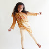 A smiling young girl with curly hair poses playfully in front of a white background, wearing a brown top, cream leggings, and Sarah's Silks Animal Print Playsilk - Fawn draped across her shoulder.