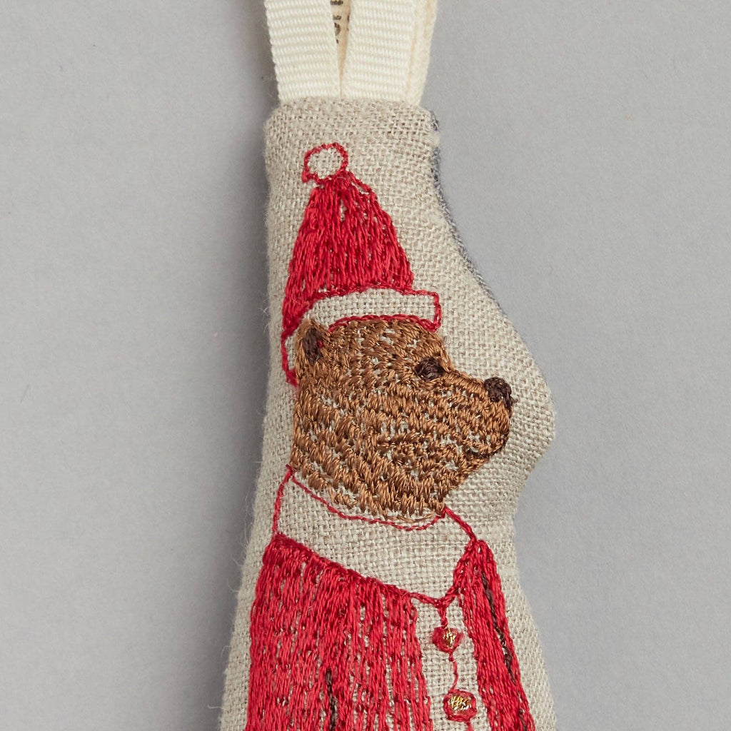 The Santa Bear Ornament showcases an embroidered bear in a striking red suit on beige fabric, complete with a looped handle, making it an ideal addition for adding festive charm to your Christmas tree.