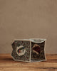 The Coral & Tusk Birdhouse Tissue Box Cover, a small rectangular embroidered cover with playful animal designs, rests on its side atop a wooden surface against a beige textured wall.
