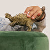 A child’s hand holds the Schleich Ankylosaurus Realistic Dinosaur Toy on a green, plush surface. Wearing a light shirt with blue dinosaur prints, the child adds extra fun and imagination to this educational playtime adventure.