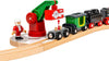 The BRIO World Christmas Steaming Train Set features a red and green crane lifting a gift onto a carriage, with a Santa figure standing on the track beside the black and red steaming train engine and carriages.