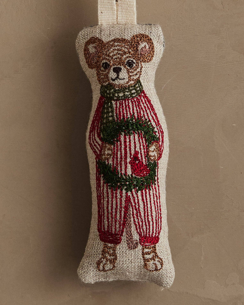 Coral & Tusk Mouse with Wreath Ornament: An embroidered mouse in red striped pajamas and green scarf, holding an evergreen wreath with a red bird, set against a neutral background.