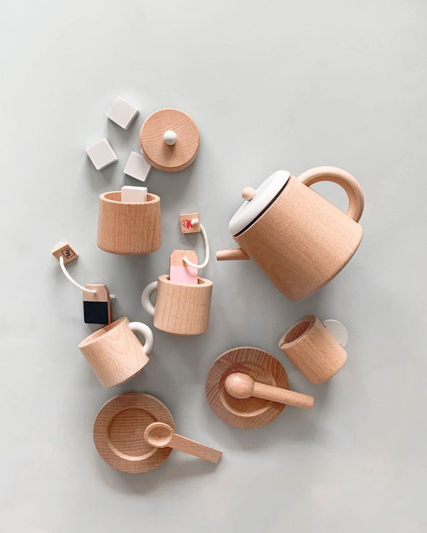 A flat lay of the Wooden Tea Set on a light gray background showcases mugs, a teapot, saucers, and spoons. Enhanced with faux tea bags and sugar cubes, the minimalist design evokes memories of enjoying a chai latte at home.