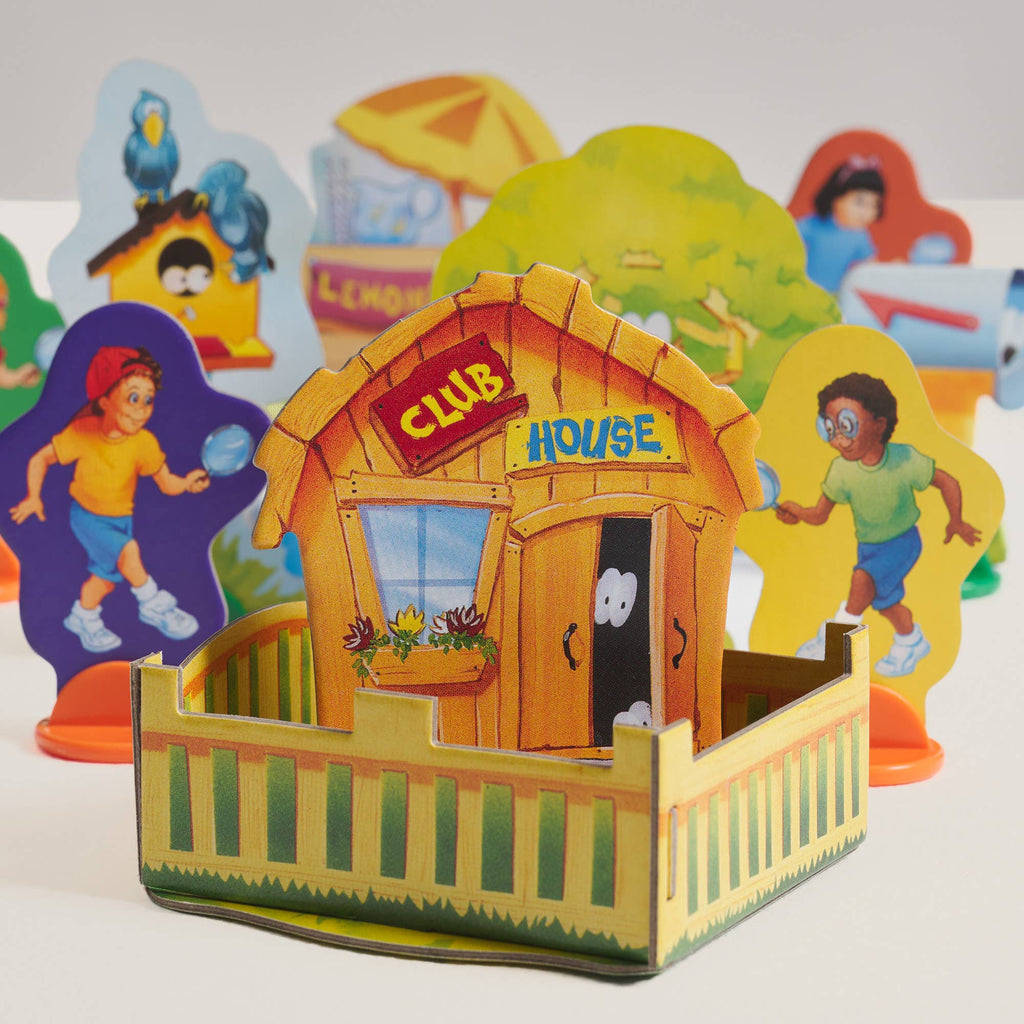 A cardboard clubhouse with a fence in the foreground, surrounded by die-cut character standees and game pieces from a Clue Jr. Vintage Bookshelf Edition mystery board game.