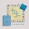 Scrabble for Juniors Vintage Bookshelf Edition featuring a blue book-shaped box, a square letter board with words placed on the grid, and a blue drawstring bag containing letter tiles.