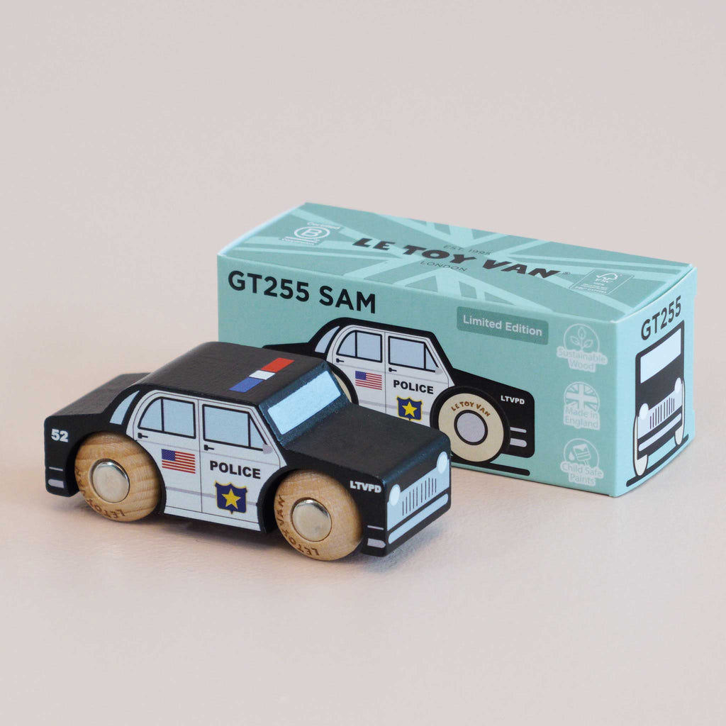 A classic toy, the No. 41 GT255 Sam black wooden police car, made in England and featuring USA and police logos, is displayed in front of a mint green box labeled “GT255 SAM” and “Limited Edition.” Perfect for imaginative play, both the car and the box showcase matching designs.