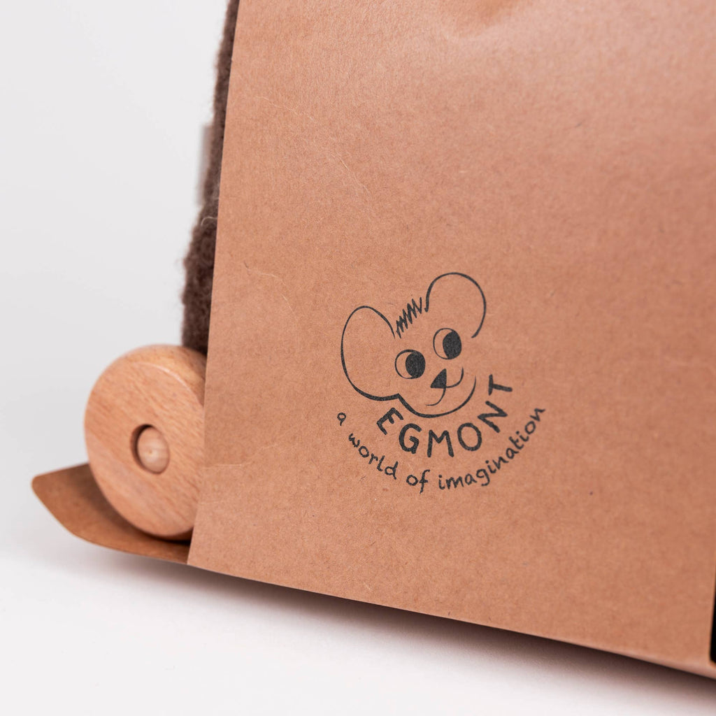 A close-up of brown packaging with a wooden wheel and a logo featuring a cartoon mouse face and the text “EGMONT a world of imagination.” Perfect for fans of Egmont Toys, this charming design hints at the whimsy found in their Pull-Along Raoul.