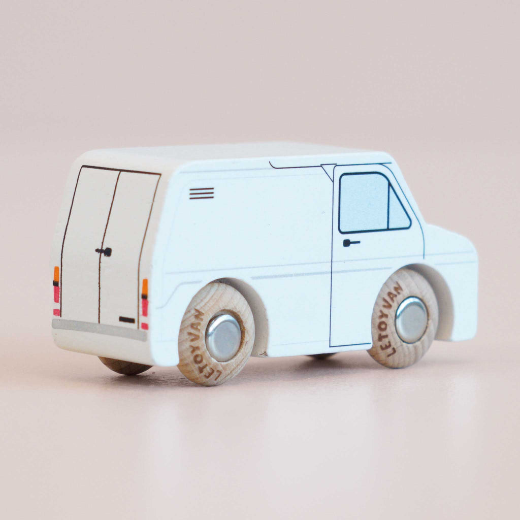 Introducing the No. 32 GT175 Frank, made in England—a classic wooden toy van with a minimalistic design. This small white vehicle showcases simple black and blue line details and wooden wheels, making it perfect for inspiring imaginative play on a light pink surface.